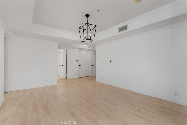 spare room with a notable chandelier, crown molding, a tray ceiling, and light hardwood / wood-style flooring