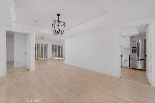 unfurnished living room with a tray ceiling, ornamental molding, a notable chandelier, and light wood-type flooring