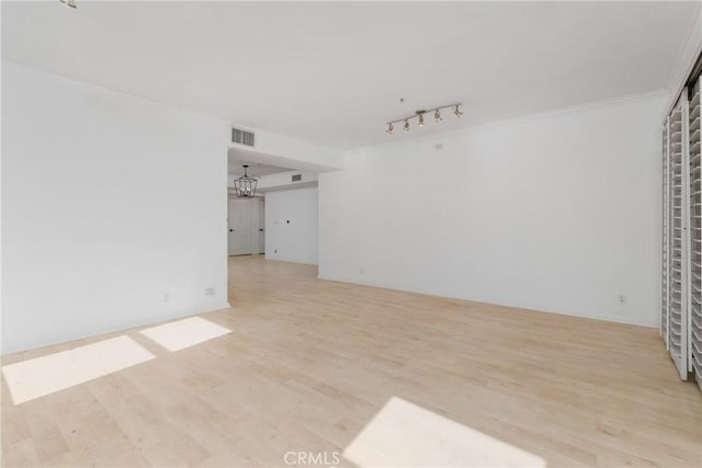 empty room with light wood-type flooring, track lighting, and crown molding