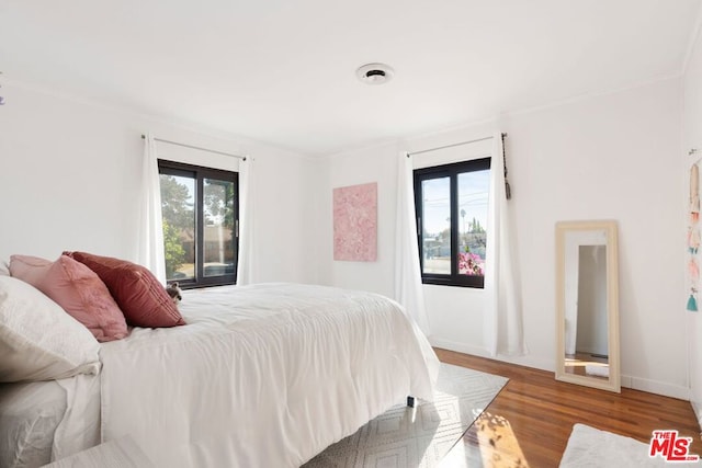 bedroom featuring multiple windows, dark hardwood / wood-style floors, and ornamental molding