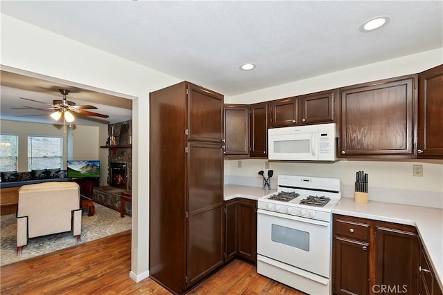 kitchen featuring dark brown cabinetry, ceiling fan, light hardwood / wood-style floors, white appliances, and a fireplace