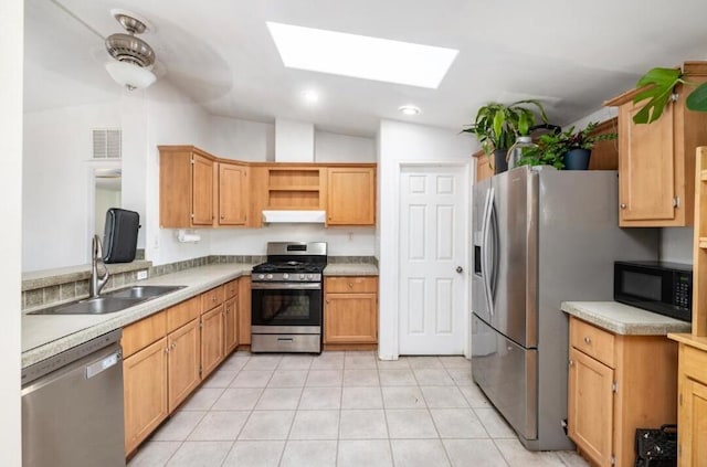 kitchen featuring ceiling fan, lofted ceiling with skylight, sink, appliances with stainless steel finishes, and light tile patterned floors