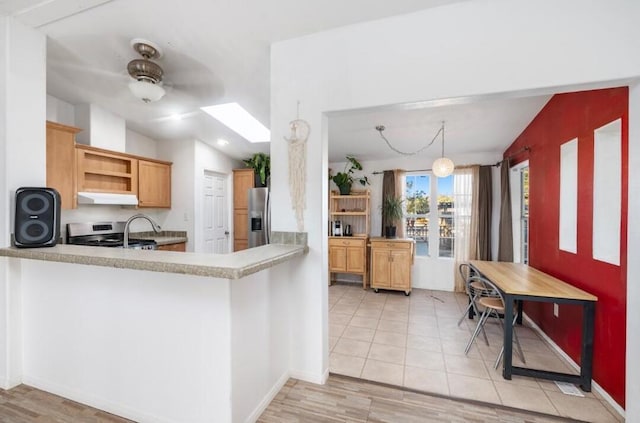 kitchen with ceiling fan, vaulted ceiling with skylight, kitchen peninsula, and stainless steel appliances