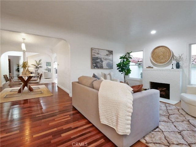 living area with arched walkways, a fireplace, recessed lighting, baseboards, and hardwood / wood-style flooring