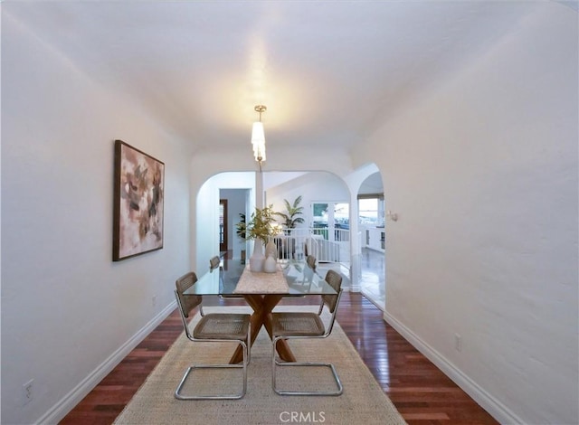 dining space featuring baseboards, arched walkways, and dark wood-type flooring