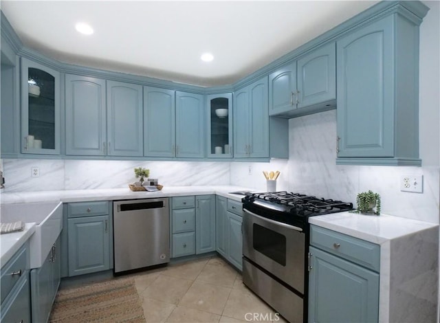 kitchen with stainless steel appliances, decorative backsplash, blue cabinetry, and light tile patterned floors