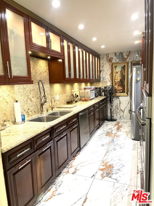 kitchen featuring decorative backsplash, light stone countertops, sink, and appliances with stainless steel finishes