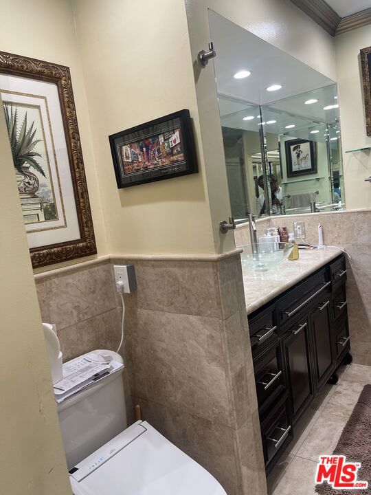 bathroom with tile patterned floors, vanity, ornamental molding, and tile walls