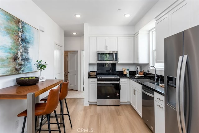 kitchen featuring dark stone counters, stainless steel appliances, sink, light hardwood / wood-style flooring, and white cabinetry