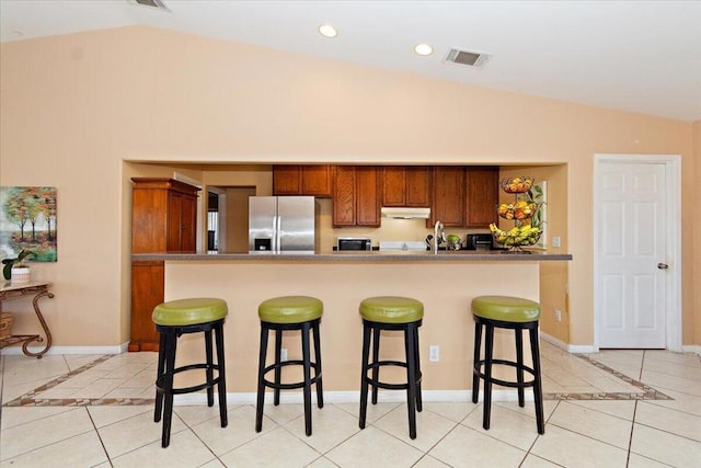 kitchen featuring a kitchen bar, stainless steel fridge with ice dispenser, vaulted ceiling, and light tile patterned flooring