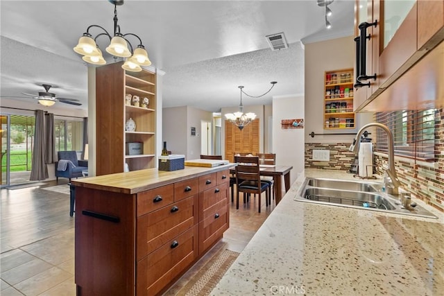kitchen featuring wooden counters, ceiling fan with notable chandelier, sink, a textured ceiling, and decorative light fixtures