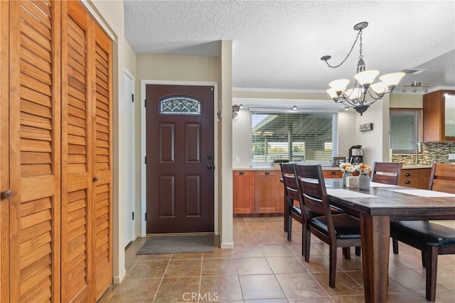 dining area with dark tile patterned flooring, a textured ceiling, an inviting chandelier, and crown molding