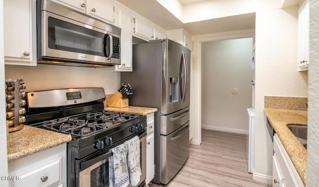 kitchen featuring sink, light stone counters, appliances with stainless steel finishes, white cabinets, and light wood-type flooring