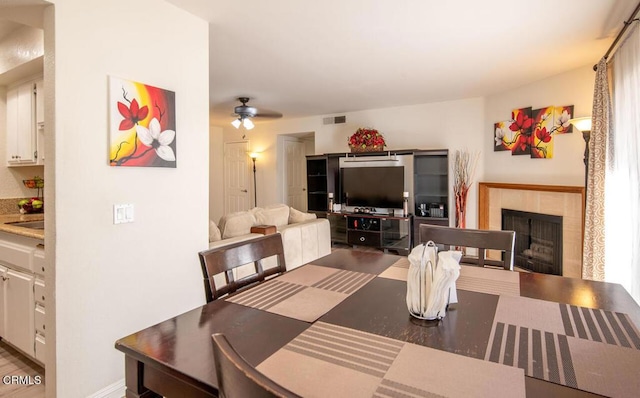 dining area featuring a tile fireplace and ceiling fan