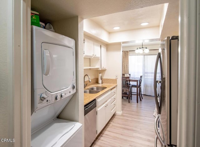 kitchen featuring sink, stainless steel appliances, stacked washer / dryer, light hardwood / wood-style floors, and white cabinets