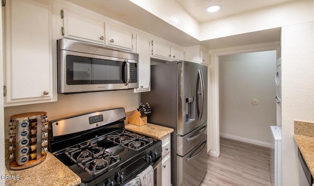 kitchen with white cabinets, light hardwood / wood-style floors, light stone counters, and appliances with stainless steel finishes