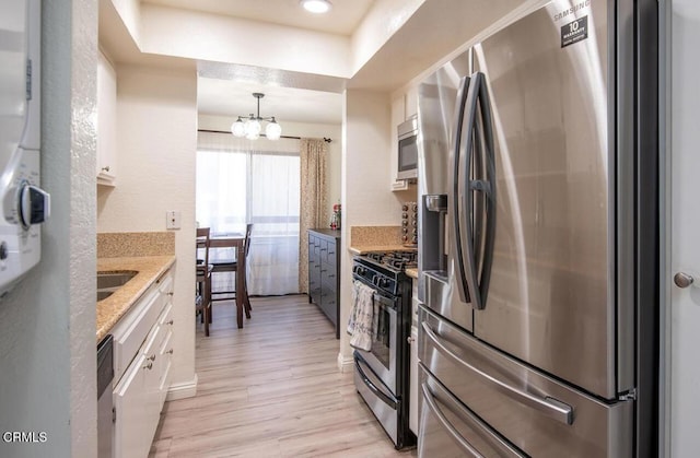 kitchen featuring decorative light fixtures, light wood-type flooring, white cabinetry, and appliances with stainless steel finishes