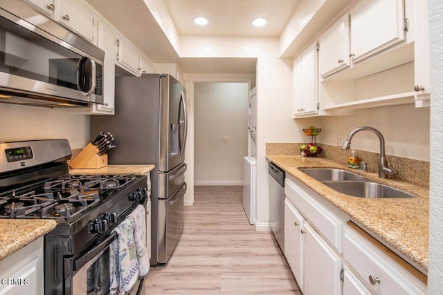 kitchen with sink, light stone counters, light hardwood / wood-style flooring, white cabinets, and appliances with stainless steel finishes