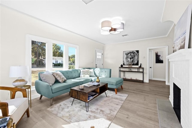 living room with light hardwood / wood-style flooring, ornamental molding, and a brick fireplace