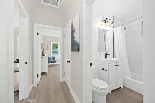 full bathroom with vanity, vaulted ceiling, shower / bath combo with shower curtain, hardwood / wood-style floors, and toilet