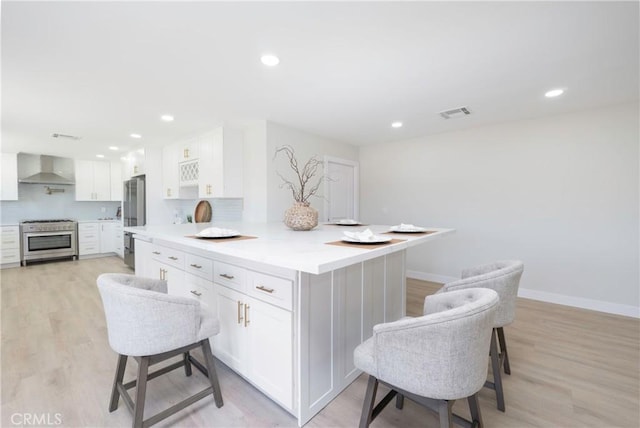 kitchen featuring wall chimney exhaust hood, white cabinetry, stainless steel appliances, and light hardwood / wood-style flooring