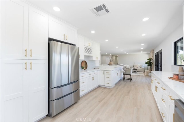 kitchen featuring white cabinets, light wood-type flooring, light stone counters, appliances with stainless steel finishes, and a kitchen bar