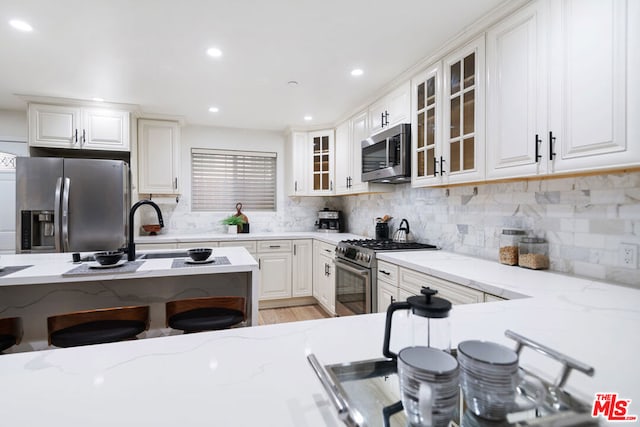 kitchen featuring backsplash, light stone counters, stainless steel appliances, sink, and white cabinetry