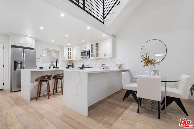 kitchen featuring light wood-type flooring, backsplash, stainless steel appliances, white cabinets, and a breakfast bar area