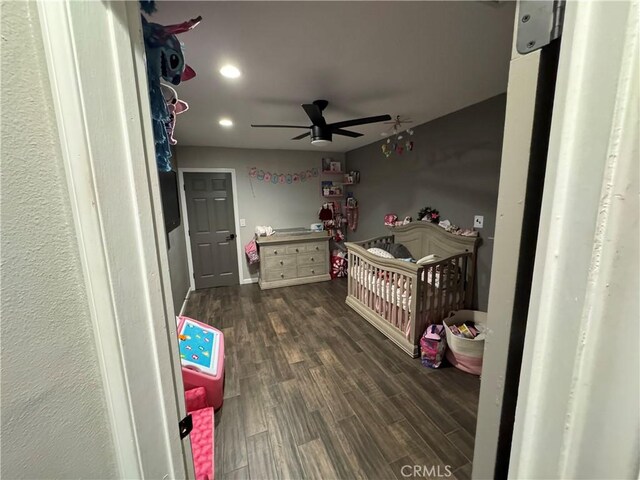 bedroom featuring ceiling fan, a nursery area, and dark hardwood / wood-style floors