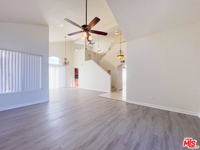 unfurnished living room with high vaulted ceiling, wood-type flooring, and ceiling fan with notable chandelier