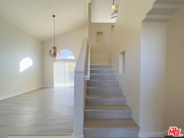 staircase featuring hardwood / wood-style flooring, high vaulted ceiling, and an inviting chandelier