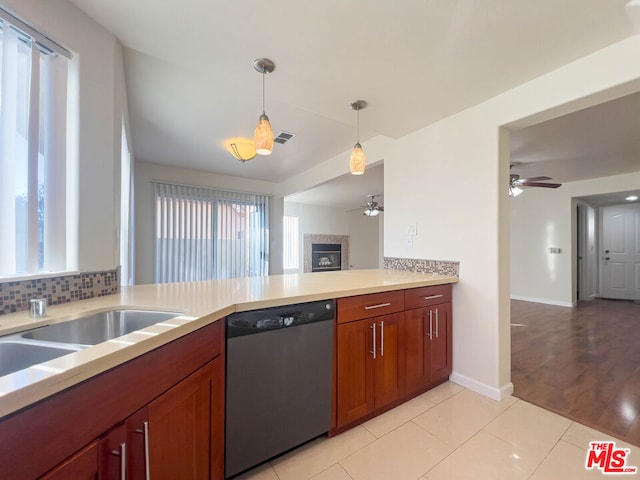 kitchen featuring backsplash, stainless steel dishwasher, light wood-type flooring, a fireplace, and decorative light fixtures