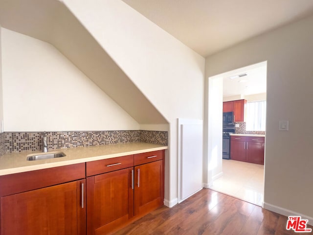 kitchen with hardwood / wood-style floors, decorative backsplash, black appliances, and sink