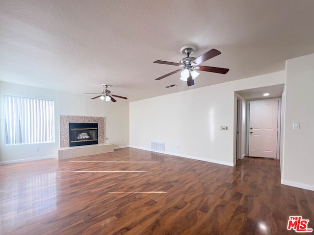 unfurnished living room with a textured ceiling, ceiling fan, a fireplace, and dark hardwood / wood-style floors