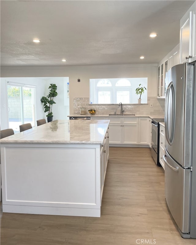 kitchen featuring a kitchen breakfast bar, sink, appliances with stainless steel finishes, light stone counters, and white cabinetry