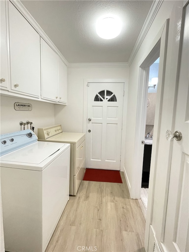 washroom with washing machine and clothes dryer, cabinets, light hardwood / wood-style flooring, crown molding, and a textured ceiling