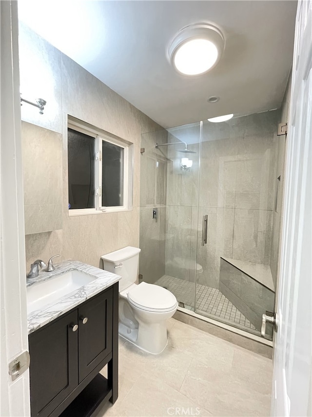 bathroom with walk in shower, tile patterned flooring, toilet, vanity, and tile walls