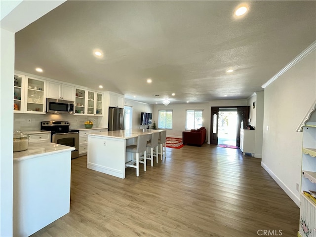 kitchen featuring a center island, white cabinets, light hardwood / wood-style flooring, appliances with stainless steel finishes, and a breakfast bar area