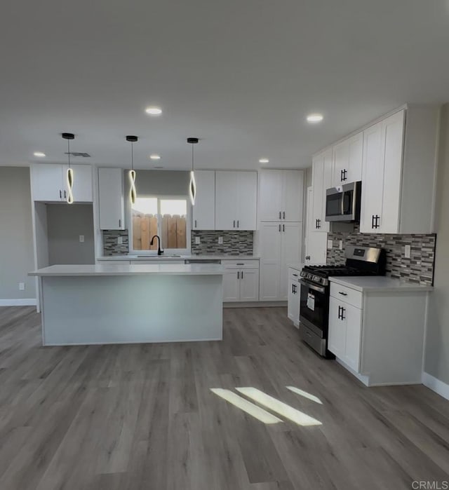 kitchen featuring white cabinets, stainless steel appliances, a kitchen island, and light hardwood / wood-style floors