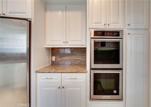 kitchen with backsplash, light stone counters, white cabinets, and stainless steel appliances