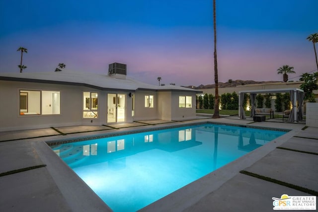 pool at dusk with a patio and central AC