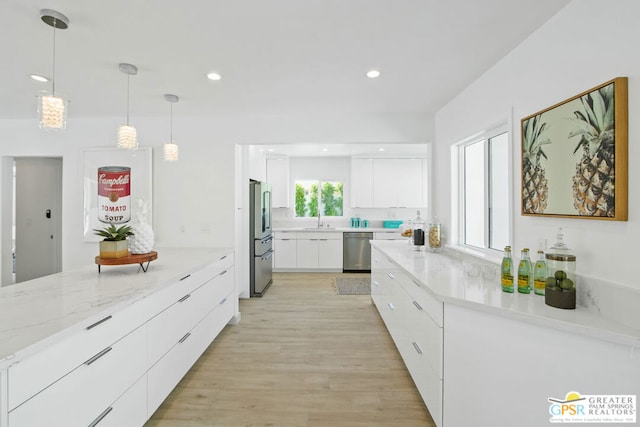 kitchen with sink, light wood-type flooring, appliances with stainless steel finishes, decorative light fixtures, and white cabinetry