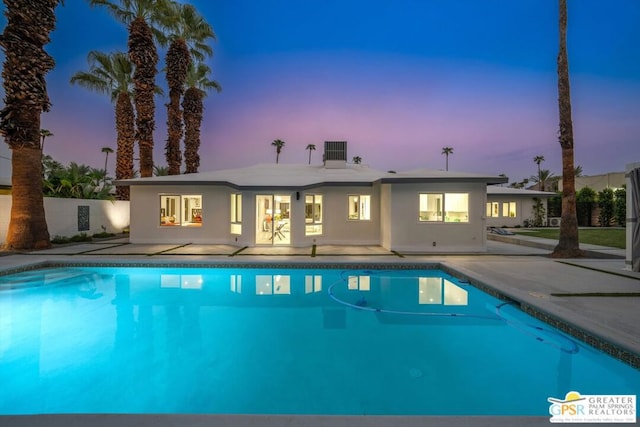 pool at dusk featuring a patio and cooling unit