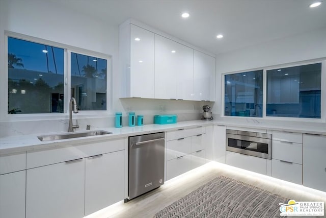 kitchen featuring white cabinets, sink, light stone countertops, light wood-type flooring, and appliances with stainless steel finishes