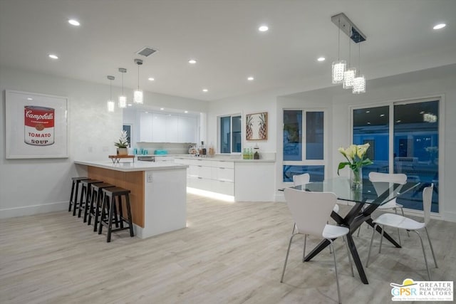 kitchen featuring kitchen peninsula, light hardwood / wood-style flooring, white cabinets, hanging light fixtures, and a breakfast bar area