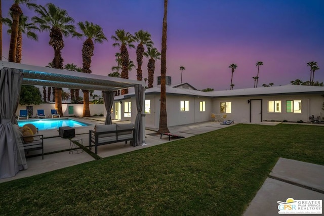 back house at dusk featuring a lawn and a patio