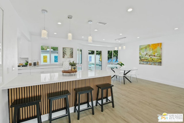 kitchen featuring a breakfast bar, pendant lighting, light hardwood / wood-style floors, and white cabinetry