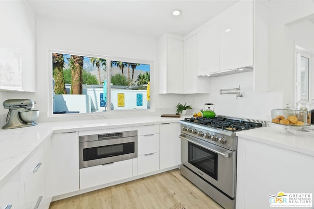 kitchen featuring light stone countertops, white cabinets, light wood-type flooring, and appliances with stainless steel finishes