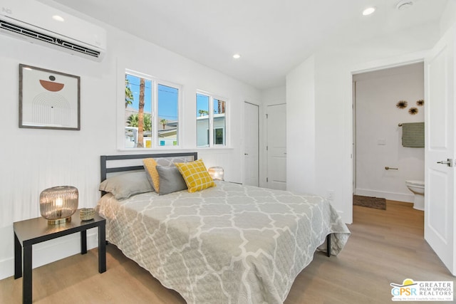 bedroom featuring light hardwood / wood-style floors, connected bathroom, and a wall mounted AC