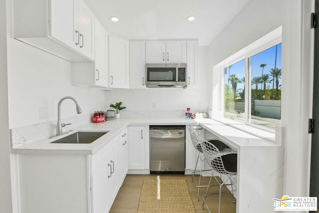 kitchen with white cabinets, sink, light stone countertops, appliances with stainless steel finishes, and light hardwood / wood-style floors